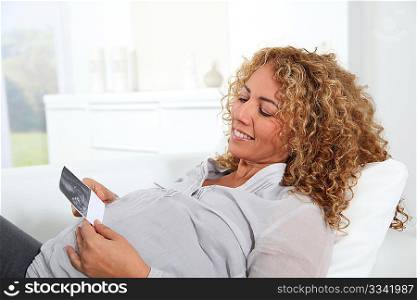 Pregnant woman laying on sofa with sonogram of future child