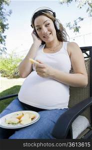 Pregnant woman listening to music and eating apple outdoors