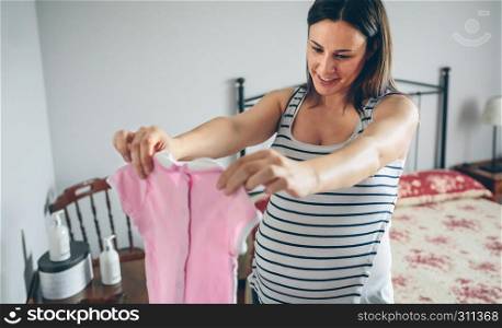 Pregnant woman looking baby girl dress. Selective background focus on woman. Pregnant looking baby girl dress