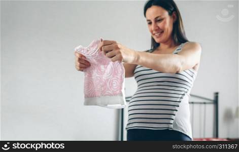 Pregnant woman looking baby girl dress. Selective foreground focus on dress. Pregnant looking baby girl dress