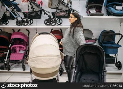 Pregnant woman looking for pushchair in store of goods for newborns. Future mother choosing stroller for her child
