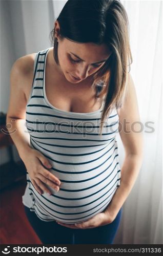 Pregnant woman looking her belly in front of a curtain. Pregnant woman looking her belly