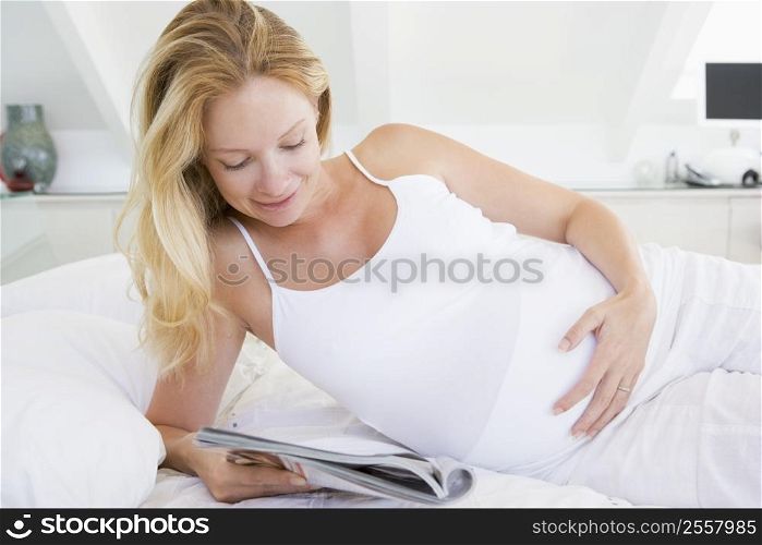 Pregnant woman lying in bed reading magazine smiling
