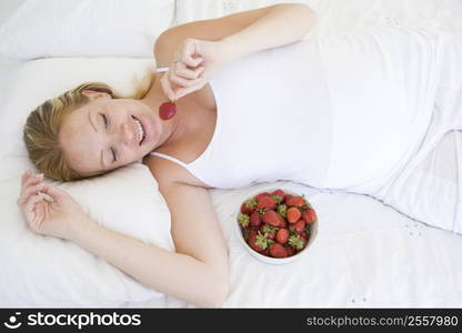 Pregnant woman lying in bed with bowl of strawberries smiling