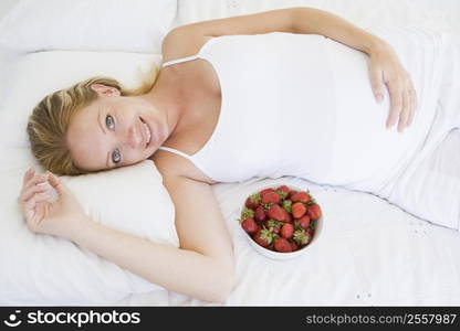 Pregnant woman lying in bed with bowl of strawberries smiling