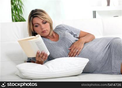 Pregnant woman lying on a couch reading a book