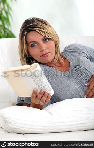 Pregnant woman lying on a sofa reading a novel