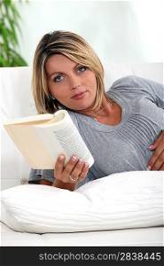 Pregnant woman lying on a sofa reading a novel