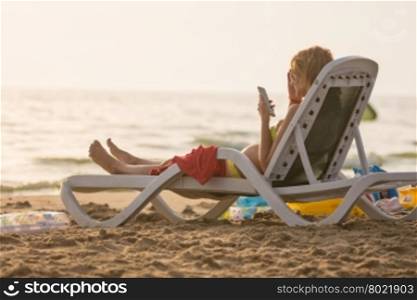 Pregnant woman lying on a sun lounger on the beach and looking at the phone