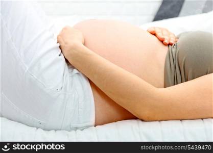 Pregnant woman lying on sofa at home and holding her belly. Close-up.&#xA;
