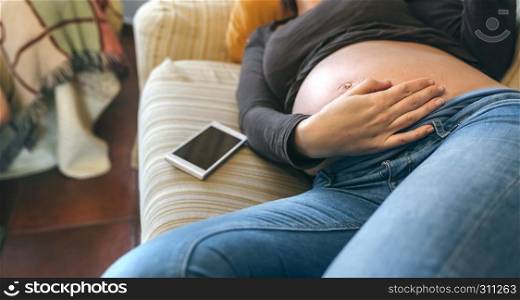 Pregnant woman lying on the couch caressing her belly in the living room. Pregnant lying on the couch caressing her belly