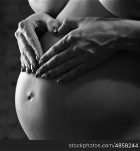 Pregnant woman making love sign over his stomach. Studio black and white female portrait
