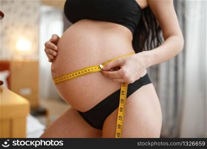 Pregnant woman measuring her belly at home. Pregnancy, calm in prenatal period. Expectant mom resting in bedroom, healthy lifestyle. Pregnant woman measuring her belly