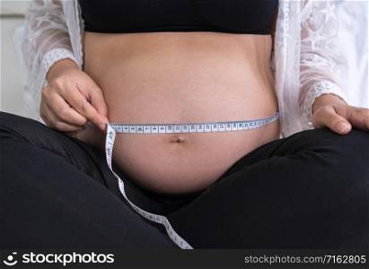 Pregnant woman measuring her belly with measure tape