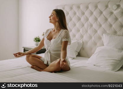 Pregnant woman meditating and practicing yoga in her bedroom in the morning