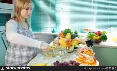 Pregnant woman mixing fruit salad in the kitchen