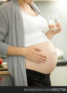 Pregnant woman on third trimester posing with glass of water on kitchen