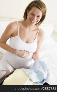 Pregnant woman packing baby clothing in suitcase smiling