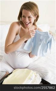 Pregnant woman packing baby clothing in suitcase smiling