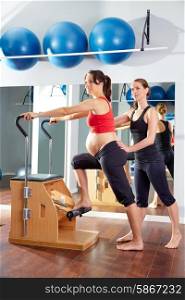 pregnant woman pilates exercise wunda chair at gym with personal trainer