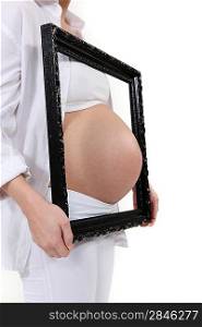Pregnant woman poking belly through picture frame