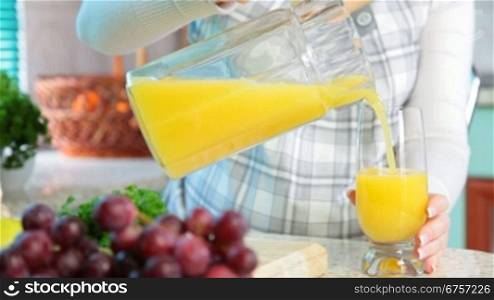 Pregnant woman pouring orange juice in the kitchen near a lot of vegetables and fruits