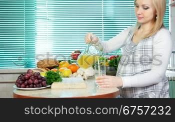 Pregnant woman pouring orange juice in the kitchen near a lot of vegetables and fruits