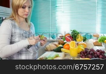 Pregnant woman preparing fruit salad slicing kiwi