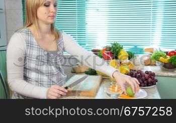Pregnant woman preparing fruit salad slicing kiwi