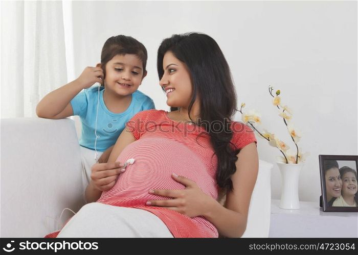 Pregnant woman putting earphone on stomach