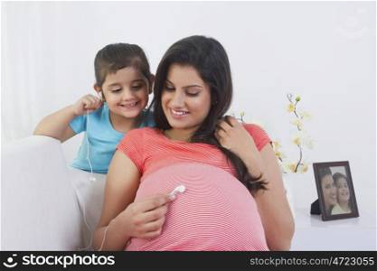 Pregnant woman putting earphone on stomach