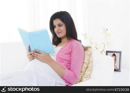 Pregnant woman reading a book on a couch