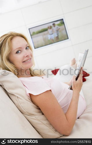 Pregnant woman reading magazine with television in background smiling