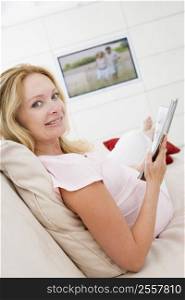 Pregnant woman reading magazine with television in background smiling