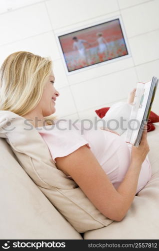 Pregnant woman reading magazine with television in background smiling