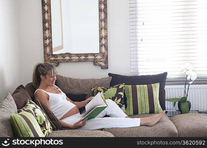 Pregnant woman reclining on sofa with book