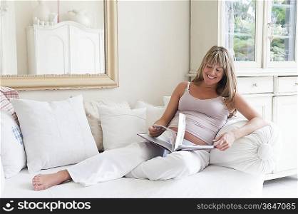 Pregnant woman reclining on sofa with book
