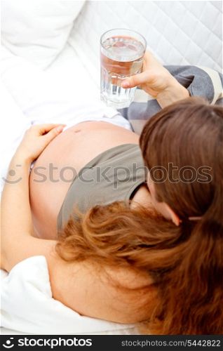Pregnant woman relaxing on sofa at home with glass of water in hand. Close-up.&#xA;