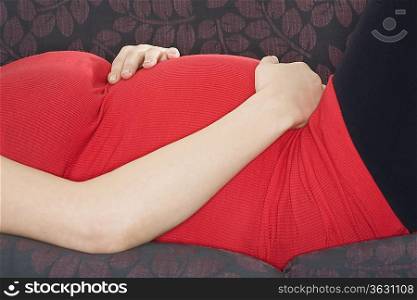 Pregnant woman relaxing on sofa, mid section
