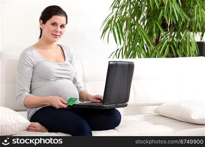 Pregnant woman sat on couch shopping on-line