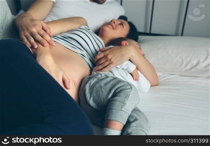 Pregnant woman sharing bed with man and little boy. Pregnant with man and boy in bed