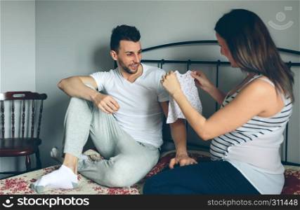 Pregnant woman showing baby dress to her husband. Pregnant showing dress to her husband