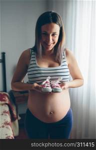 Pregnant woman showing baby sneakers in bedroom. Pregnant showing baby sneakers