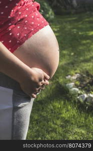 Pregnant woman shows his belly. In the nature. Green meadow