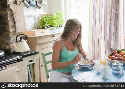 Pregnant woman sitting at kitchen table eating breakfast