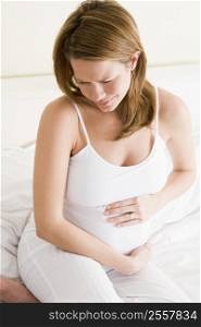 Pregnant woman sitting in bed holding stomach in pain