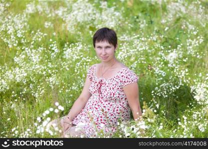 Pregnant woman sitting in chamomile background