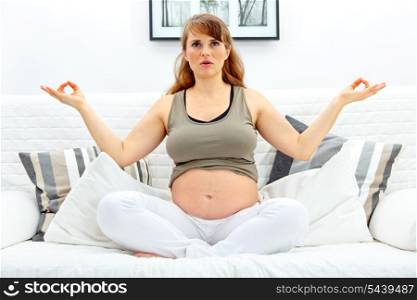 Pregnant woman sitting in meditating on sofa at home.&#xA;