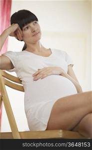 Pregnant woman sitting on chair and looking away