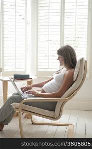Pregnant woman sitting on chair using laptop